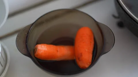 Two fresh carrots soaking in dark liquid inside bowl. Stock Footage 330942673