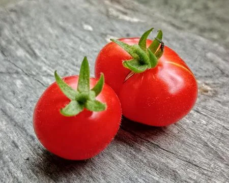Two Fresh Cherry Tomatoes With Green Calyxes On Rustic Wooden Surface Stock Photos