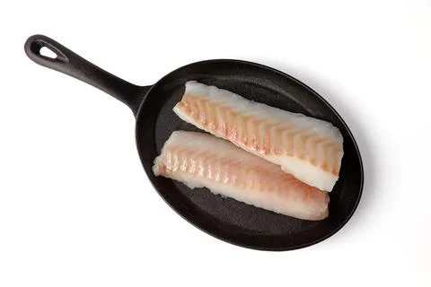 Two fresh cod fish fillets on black cast iron frying pan isolated on white .. Stock Photos