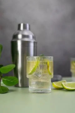 Two fresh cold glasses of mahito with lime and ice and shaker on a gray-green Stock Photos