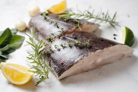 Two fresh halibut fish pieces with herbs and lemon Stock Photos