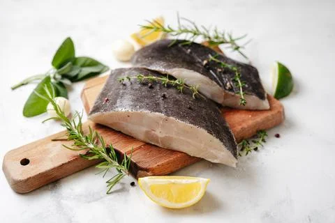 Two fresh halibut fish pieces with herbs and lemon Stock Photos