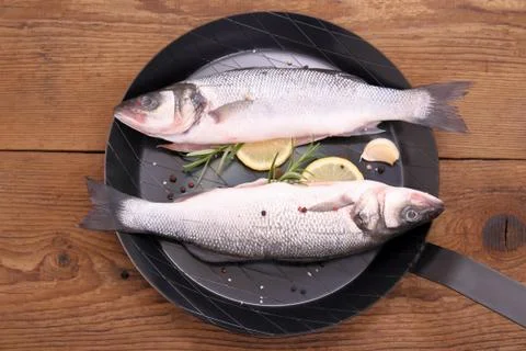 Two fresh moronidae fish on frying pan with ingredient Stock Photos