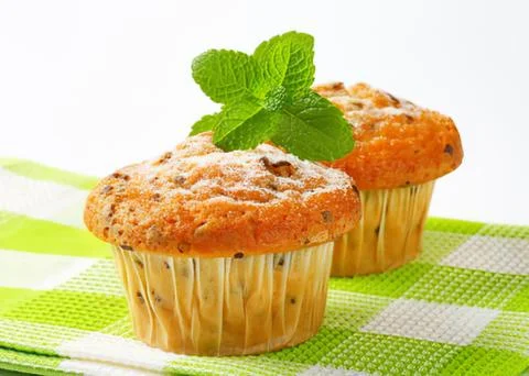 Two fresh muffins with mint leaf garnish on green table Stock Photos