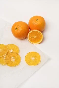 Two fresh oranges, next to which are dried orange slices on parchment paper. Stock Photos