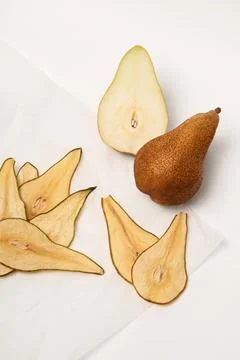 Two fresh pears, next to which are dried slices of pears on parchment paper. Stock Photos