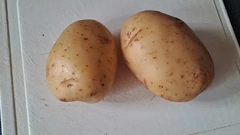 Two fresh raw potatoes sitting on white cutting board video motion Stock Footage 339505155