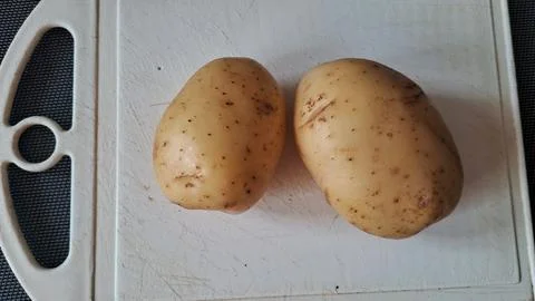 Two fresh raw potatoes sitting on a scratched white plastic board Fotos de archivo