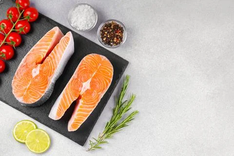 Two fresh raw salmon steaks with tomatoes, spices, rosemary and lime on whi.. Stock Photos