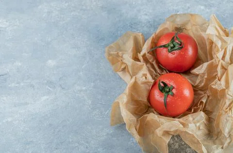 Two fresh whole tomatoes on a parchment paper Stock Photos