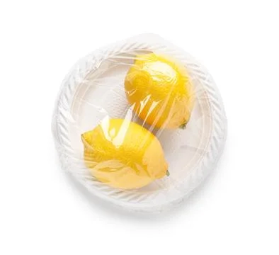 Two fresh yellow lemons wrapped in plastic film on a disposable white plate,  Stock Photos