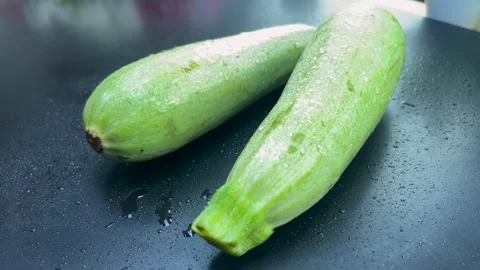 Two fresh zucchini with drops of water lie on a black kitchen table and the.. Stock Footage 286467742