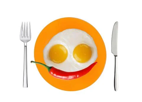 Two fried eggs and red hot chilly pepper on orange plate, knife and fork isol Stockfoto's