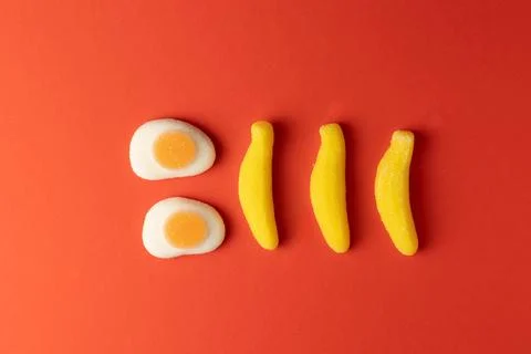 Two fried eggs and three bananas candy on red background Stock Photos