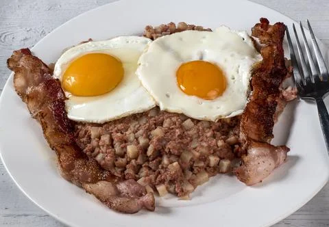 Two fried eggs  on corn beef hash  with bacon Stock Photos