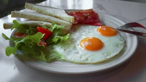 Two fried eggs, crispy bacon strips, toasted slices of bread and fresh salad Stock Footage 312742013