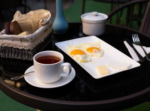 Two fried eggs, a cup of tea and cheese slices on the black table Stock Photos