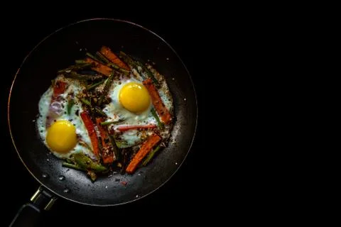 Two fried eggs in a pan with large slices of carrots, bell pepper and asparagus Stock Photos