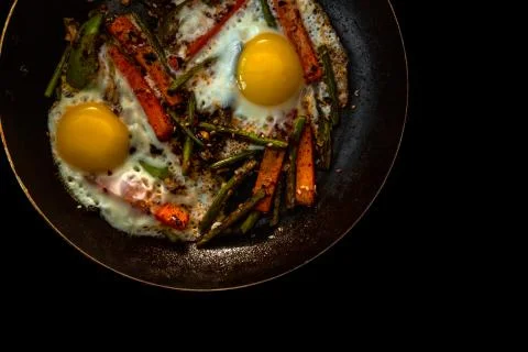 Two fried eggs in a pan with large slices of carrots, bell pepper and asparagus Stock Photos