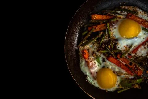 Two fried eggs in a pan with large slices of carrots, bell pepper and asparagus 写真素材