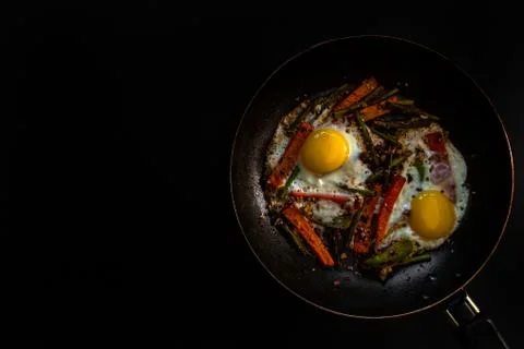 Two fried eggs in a pan with large slices of carrots, bell pepper and asparagus Stock Photos