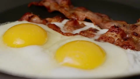Two fried eggs with pieces of fried crispy bacon in a hot frying pan. Stock Footage 170620427