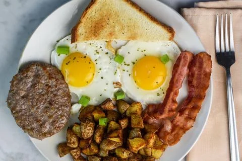 Two fried eggs served with bacon sausage and home fries Stock Photos