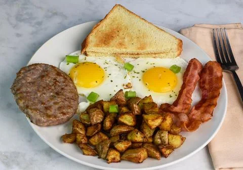 Two fried eggs served with bacon sausage and home fries Stock Photos