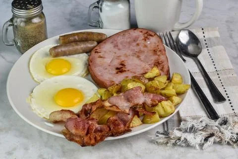 Two fried eggs  served with bacon, sausage and ham Stock Photos