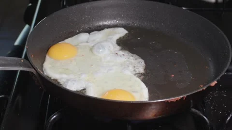 Two fried eggs sizzling in a pan on a stovetop Stock Footage 314291825