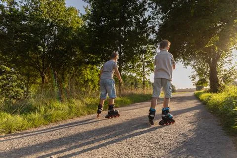 Two friends are enjoying inline skating along a gravel pathway surrounded b.. Stock Photos
