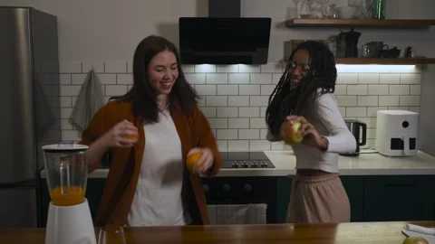 Two friends are having fun in the kitchen, juggling fruits and laughing. Stock Footage 301101355