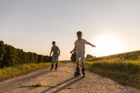 Two friends are having fun inline skating down a dirt path surrounded by tr.. Stock Photos