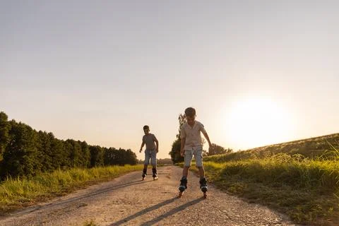 Two friends are having fun inline skating down a dirt path surrounded by gr.. Stock Photos