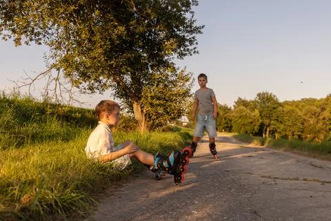 Two friends are inline skating on a warm afternoon. One child sits on the g.. Stock Photos
