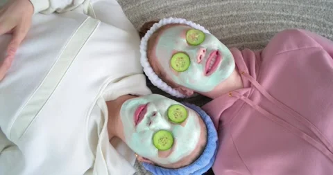 Two friends are lying on at-home carpet with mint masks and cucumber slices, Stock Footage 335365246