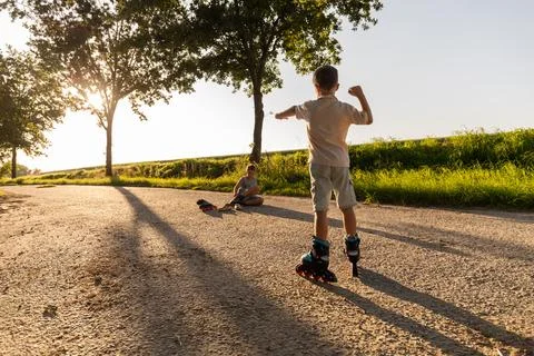 Two friends are outside roller skating along a sunny path in the park. One .. Stock Photos