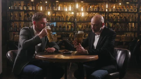 Two friends are relaxing in a pub after work on Friday. The men, dressed in Stock Footage 237597693