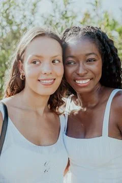 Two friends are smiling while standing together and looking around, female .. Stock Photos