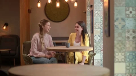 Two friends are talking in a nice cozy coffee shop, Two girls are having a Stock-Footage 135997598