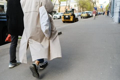Two friends are walking down street in cool weather, raincoat fluttering in wind Stock Photos