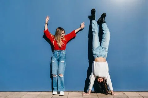Two friends a blonde and a brunette having fun on a blue wall Stock Photos