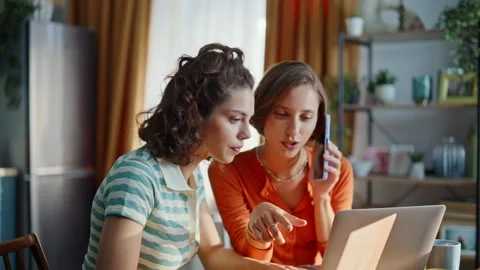 Two friends calling cellphone looking laptop at kitchen closeup. Calm brunette Stock Footage 333790914