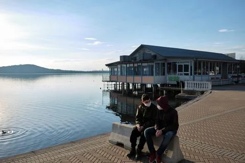 Two friends chat in front of a chalet on the lake with the anti-covid19 mask Stock Photos