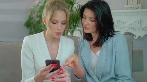 Two friends communicate with each other and look at the phone, Modern women talk Stock Footage 136510616