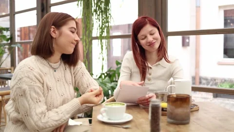 Two friends in a cozy cafe talking one girl admits she has no money while the ot Stock Footage 320827347
