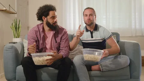Two friends from different backgrounds enjoy a cozy movie night with popcorn and Stock Footage 305504091