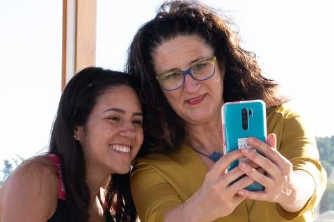 Two friends of different ethnicities sitting smiling talking on a video call. Stock Photos