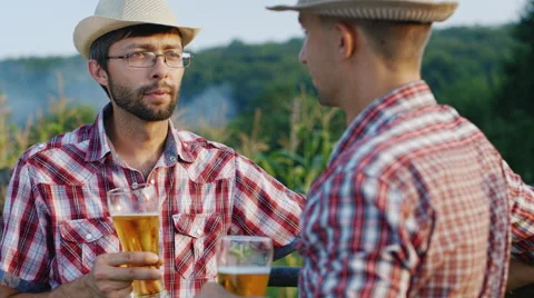Two friends drinking beer in the countryside. They are wearing hats - farmers Stock Footage 65454586