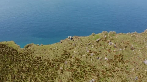 Two friends on the edge of steep cliff. Extinct volcano in ocean. Aerial of Video stock 119892047